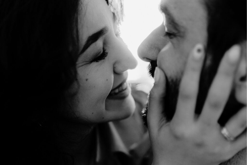 女性が男性の顔を包み込んで微笑んでいる姿。男性も微笑んでいる。とても仲の良い夫婦と見受けられる。